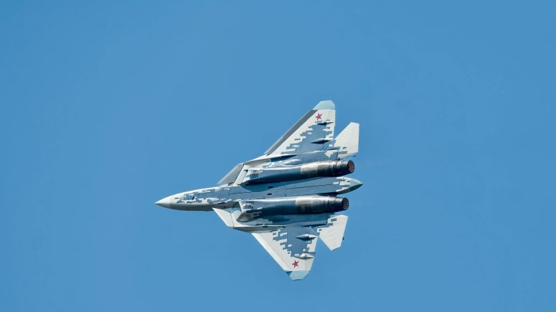 Venäläinen hävittäjälentokone Suhoi Su-57 lentämässä kirkkaalla taivaalla, kuvattuna alhaalta käsin.