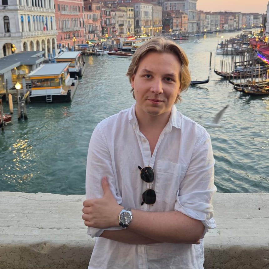 Valokuva Joona Lehtimäestä valkoisessa pellavapaidassa aurinkolasit kauluksessa nojaamassa kaiteeseen. Taustalla näkyy Venetsian Canal Grande iltahämärässä gondoleineen ja historiallisine rakennuksineen.
